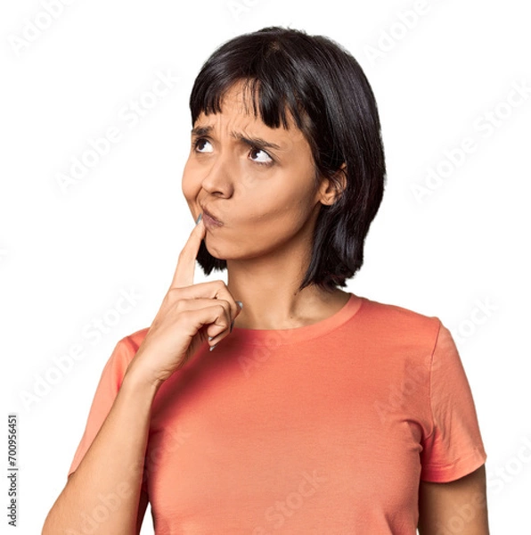 Fototapeta Young Hispanic woman with short black hair in studio looking sideways with doubtful and skeptical expression.