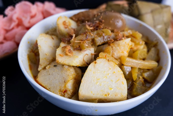 Fototapeta Ketupat Sayur or Lontong Sayur, a typical Indonesian food. Served with pumpkin vegetables, boiled eggs and tofu stew and crackers. Served during Ramadan, Eid al-Fitr and Adha. Black Background