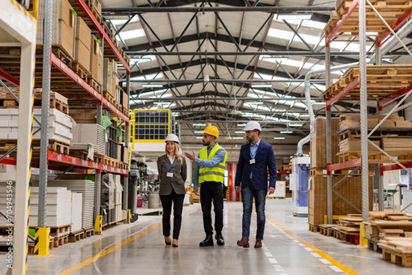 Fototapeta Engineers walking with foreman in modern industrial factory, talking about new production project or investment. Team management in manufacturing facility.