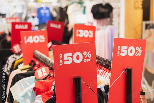 Fototapeta Red discount signs on clothes racks in a clothing store.