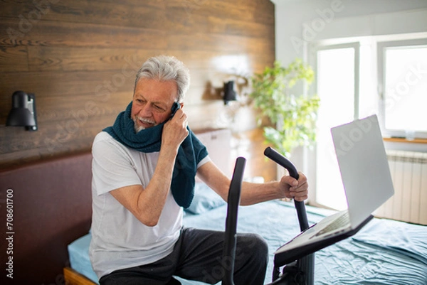 Fototapeta Senior man exercising on a fitness bike in the bedroom at home