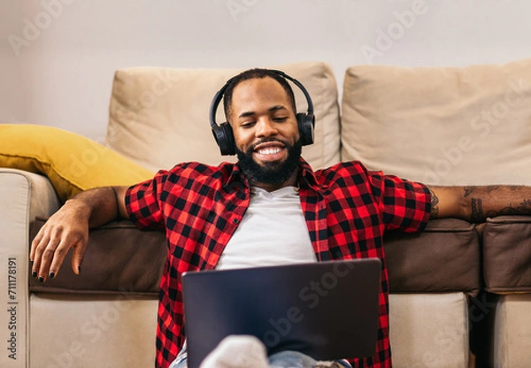 Fototapeta African american man in casual clothes using laptop at home.