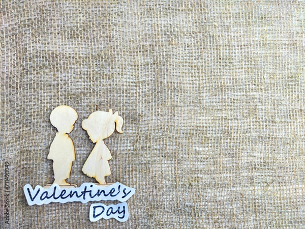 Fototapeta Wooden figurines of couple on jute background and inscription Valentine's Day. Concept of holiday. Card, Texture, Frame, place for text, copy space