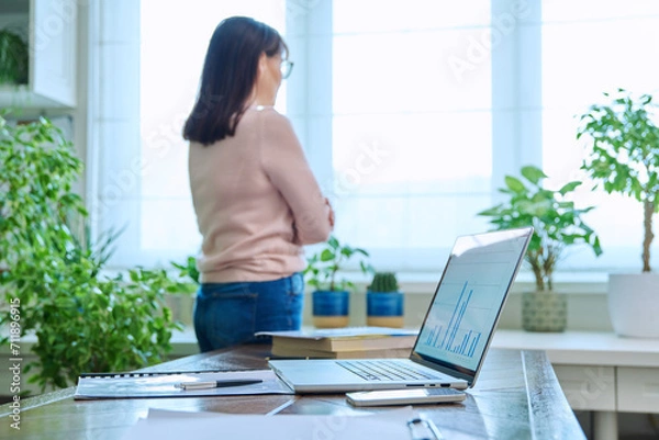 Fototapeta Home office, workplace desk with computer, out of focus woman looking out window