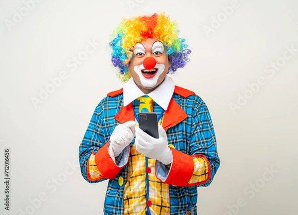 Fototapeta Mr Clown. Portrait of Funny face Clown man in colorful uniform standing holding smartphone. Happy expression male bozo in various pose with cellphone on isolated background.