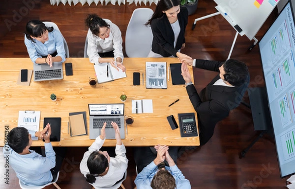 Fototapeta Two businessman shake hand in meeting room with coworker give cheerful applause. Team of analyst celebrate after successful significant progress on business strategic performance. Meticulous