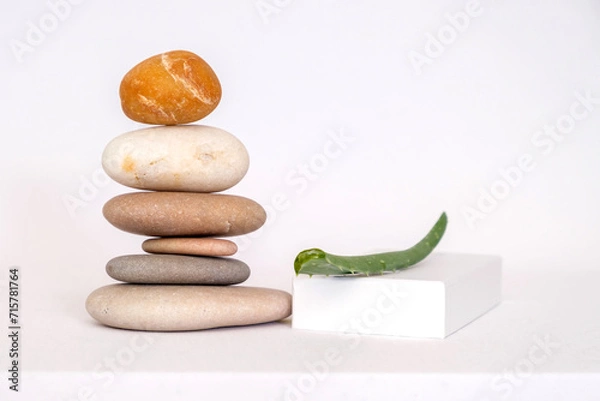 Fototapeta Pyramid of pebbles, cut aloe and podium. Isolated on white background.