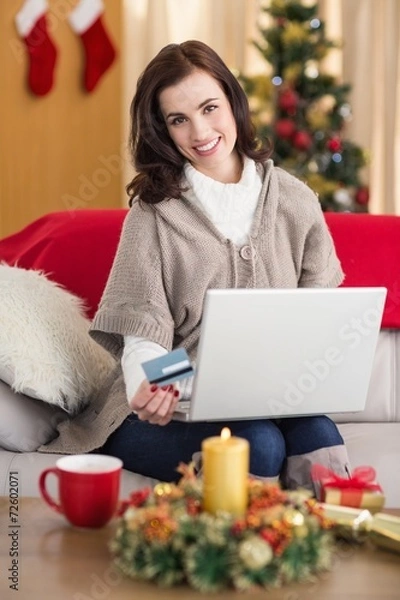 Fototapeta Smiling brunette shopping online with laptop at christmas