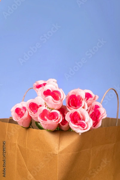 Fototapeta Bouquet of pink roses in a paper bag on blue background, valentine's day background