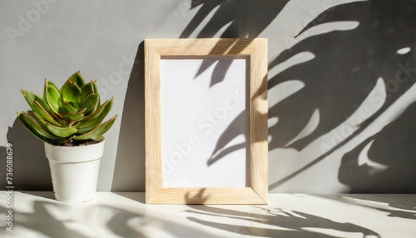 Fototapeta enhancing the mockup overlay in a horizontal, two vertical sheets of textured white paper against a soft gray table background. the natural light creates subtle shadows from an with leaves on table