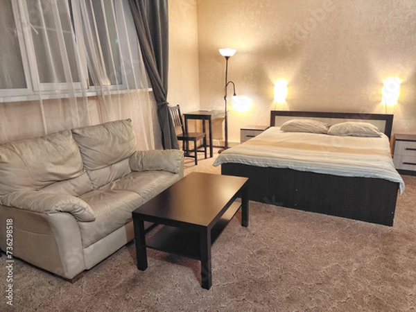 Fototapeta Stylish bedroom in beige tones and colors with double bed, sofa and table. Concept of cozy bedroom, living room or hotel room