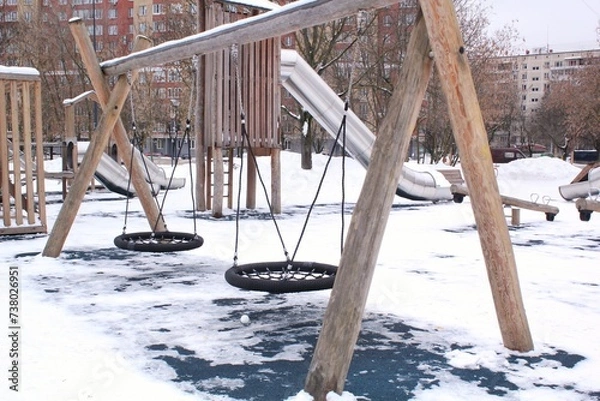 Fototapeta Wooden playground made of natural eco-friendly material in public city park with snow at winter time. Modern safety children outdoor equipment. Winter activities. Children rest and games on open air