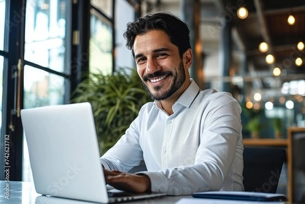 Fototapeta Happy young Latin business man looking at laptop at work. Smiling businessman professional employee, company manager using computer sitting at desk managing digital data in, Generative AI