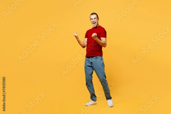 Fototapeta Full body side view young middle eastern man he wears red t-shirt casual clothes doing winner gesture celebrate clenching fists say yes isolated on plain yellow orange background. Lifestyle concept.