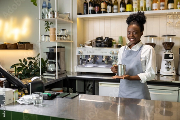 Fototapeta Smiling multicultural woman barista making coffee standing at counter in cafe