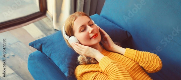 Fototapeta Happy relaxed young woman listening to music with headphones lies on couch at home