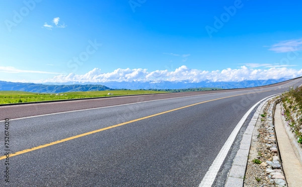 Fototapeta Asphalt highway road and green meadow with mountain nature landscape under blue sky