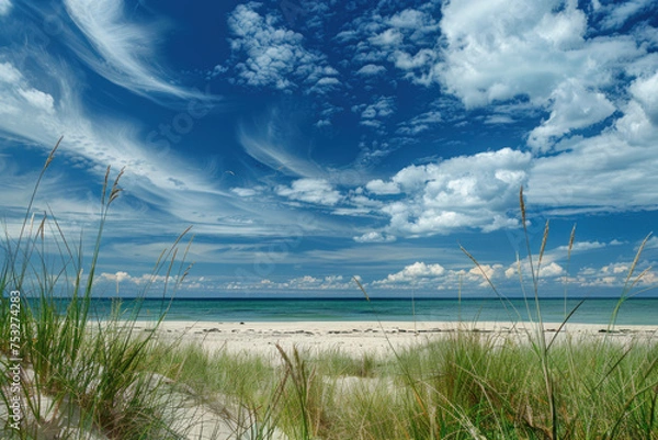 Fototapeta Pristine beach with white sand, dune grass, and a stunning blue sky with wispy clouds.