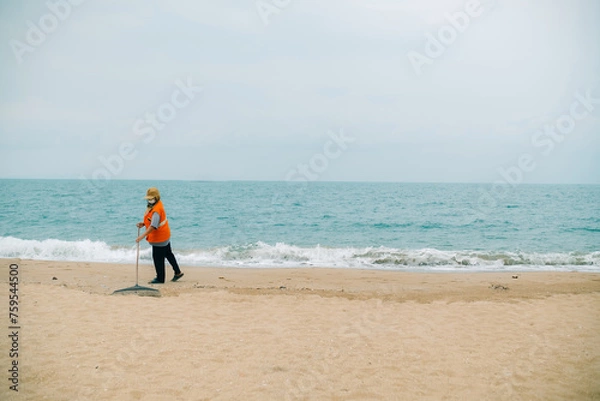 Obraz A cleaner in an orange uniform are cleaning up trash on the beach