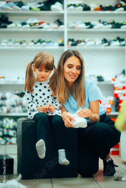 Fototapeta Daughter Trying on New Sneakers in a Shoe Store Helped by Mom. Cheerful little child having fun picking new sneakers 
