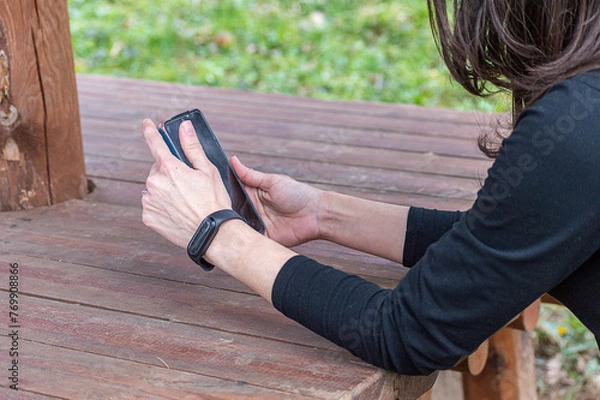 Fototapeta Woman using a cellphone in the park to read the news