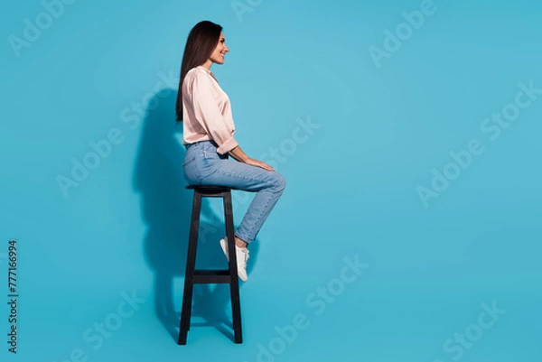 Fototapeta Full length photo of cute positive woman wear silky blouse sitting chair looking empty space isolated blue color background