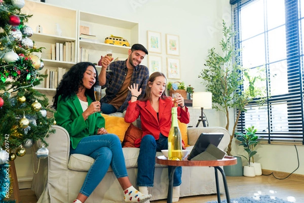 Fototapeta Group of young people toasting with champagne, enjoying a virtual get-together by a well-decorated Christmas tree.