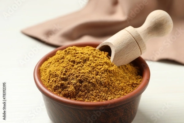 Fototapeta Curry powder in bowl and scoop on white table, closeup