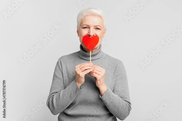 Obraz Senior woman with a paper heart covering mouth