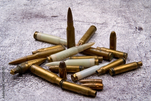 Fototapeta From above of collection of fired golden bullets and unfired cartridges with white plastic case arranged on rough floor at daytime