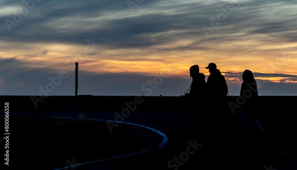 Fototapeta Three people walking in the dark with a sunset in the background