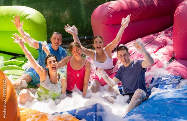 Fototapeta Happy friendly team having fun ball collecting competition in foam pool on adults bouncy playground during sunny summer weekend..