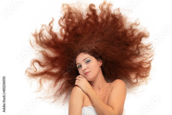 Fototapeta A young beautiful woman with scattered curly long luxurious hair on a white background.