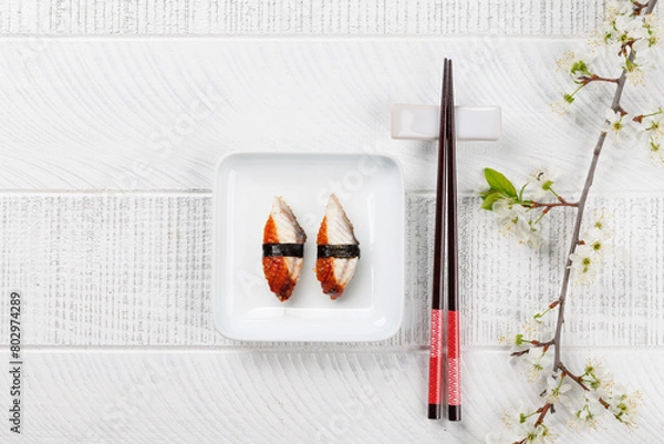 Fototapeta Eel sushi adorned with cherry blossom branch and chopsticks, epitomizing Japanese food culture