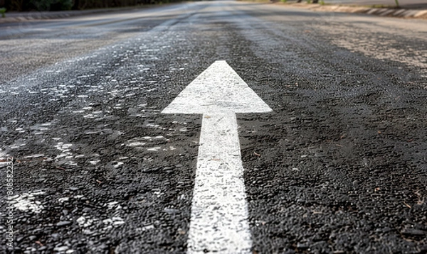 Fototapeta The asphalt road stretches towards the horizon, with a visible white arrow pointing the way ahead. It is a symbolic representation of the path to success.