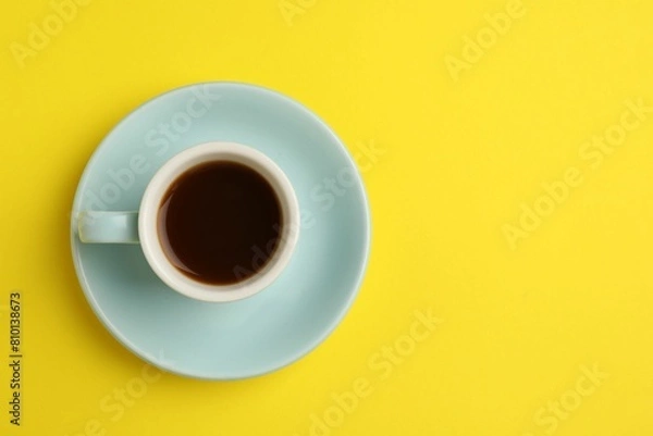 Obraz Tasty coffee in cup on yellow background, top view. Space for text