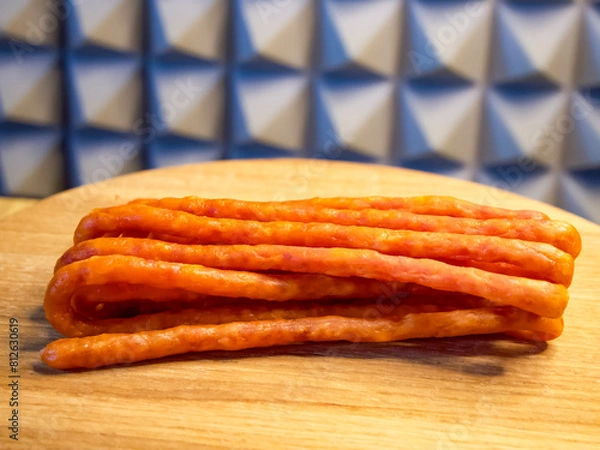 Fototapeta Sausages piled on a wooden surface, contrasting with a checkered backdrop. Ideal for showcasing in culinary presentations or grocery store promotions.