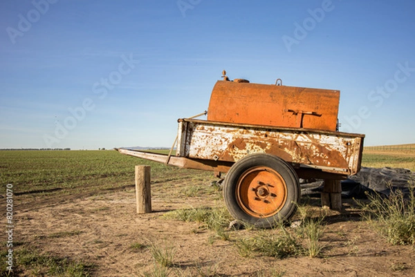 Fototapeta Decaying vintage farm equipment, a watercart, stands alone in a serene countryside landscape