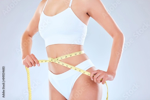 Fototapeta Body, stomach and woman with measuring tape in studio for WEIGHT LOSS, detox or diet results on grey background. Abdomen, measurement and girl model with tools for fasting, progress or slimming check