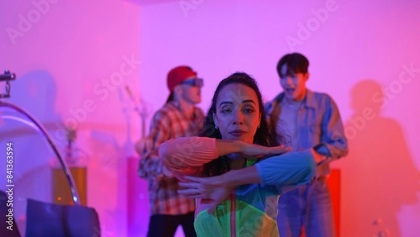 Fototapeta Attractive happy dancer looking at camera while smart woman moving at rhyme with neon light. Professional hispanic performer break dancing while wearing colorful cloth with diverse friend. Regalement.