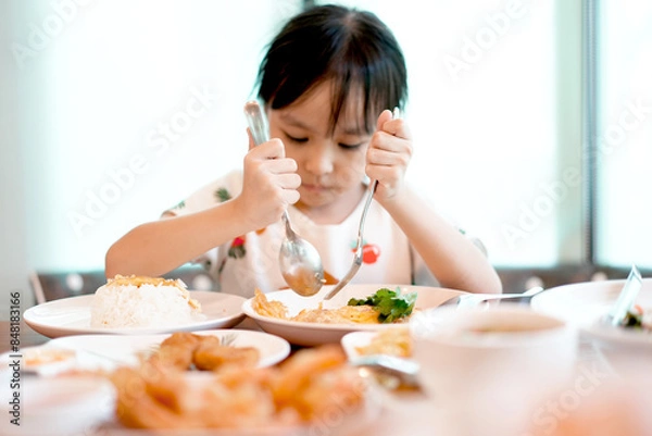 Fototapeta Cute asian kid girl eating rice with 
omelet by self. Copy space. Learning Concept .