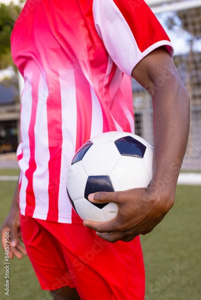 Fototapeta African American soccer player holds soccer ball, wears red and white sports uniform