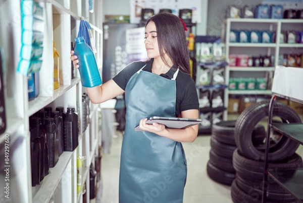 Fototapeta latin american saleswoman entrepreneur holding a digital tablet and oil container in an auto parts supply store	