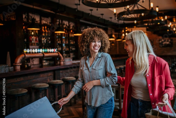 Fototapeta Two smiling female friends entering the bar with a shopping bags, laughing and talking