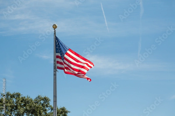 Fototapeta American Flag Blowing on Metal Pole on Blue Sky