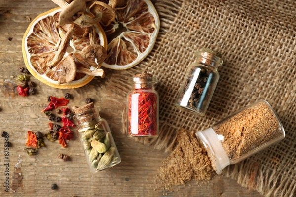 Fototapeta Assortment of spices in glass bottles on wooden background