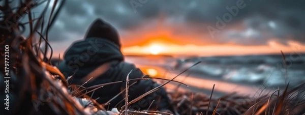 Fototapeta  A person atop a grassy field, beside a body of water, during sunset