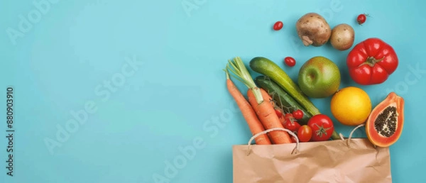 Fototapeta A rustic brown paper bag full of fresh fruits and vegetables against a turquoise backdrop, promoting a balanced and healthy lifestyle.