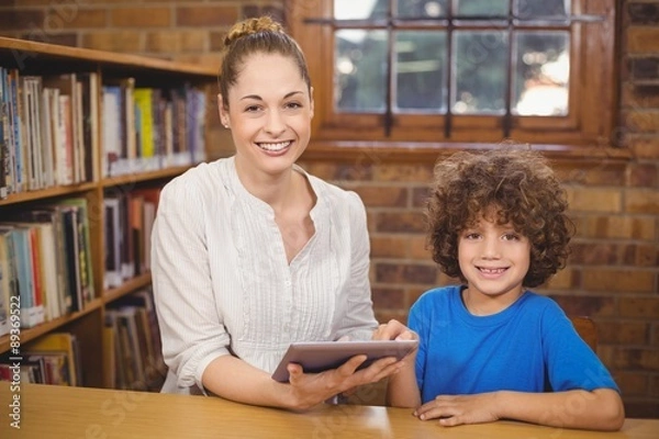 Obraz Blonde teacher and pupil using tablet in the library