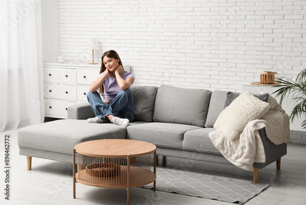 Fototapeta Pretty young woman sitting on comfortable sofa in living room